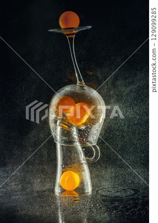 Still life with glasses and orange balls with water spray, stylization 129099285