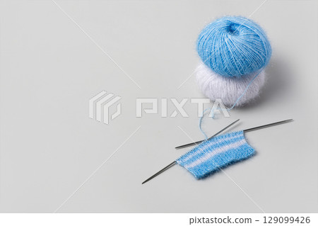 Blue and white knitted wool on gray background with knitting needles for knitting warm clothes and hobbies needlework 129099426