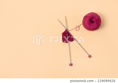 Vinous knitted wool on orange background with knitting needles for knitting warm clothes and hobbies needlework Vinous knitted wool on orange background with knitting needles for knitting warm clothes and hobbies needlework 129099428