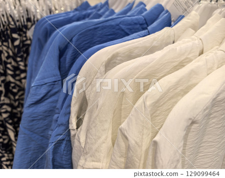Soft cotton shirts in shades of blue and white hanging in a boutique store Soft cotton shirts in shades of blue and white hanging in a boutique store 129099464
