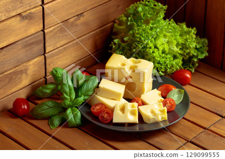Swiss cheese, green basil, salad, and tomatoes on a wooden table. Swiss cheese, green basil, salad, and tomatoes on a wooden table. 129099555