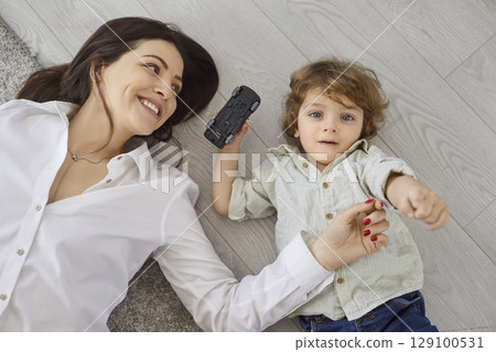 Happy mother and son lying on floor and playing together, top view of family fun time at home Happy mother and son lying on floor and playing together, top view of family fun time at home 129100531