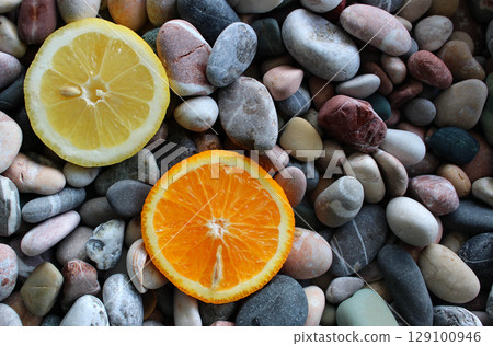 Two halves of ripe lemon and fresh orange on a sea stones at a side of image concept for logo or titles 129100946