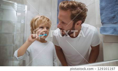 Dad teaching son dental care, sharing morning routine in bathroom mirror with toothbrushes 129101197