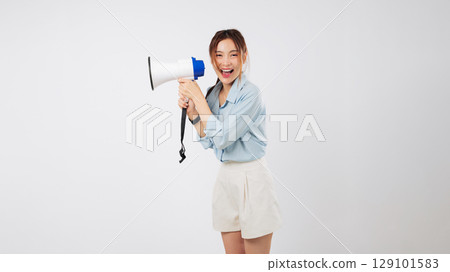 A young Asian woman is shouting into a megaphone, making an important announcement. Her mouth is wide open, actively screaming the news through her reliable megaphone. isolated studio white background 129101583