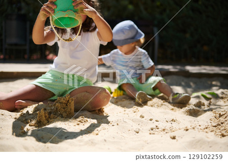 Children Playing and Building in a Sunny Sandbox During Summer 129102259