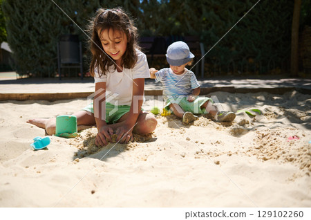 Children Playing Happily in a Sunny Playground Sandbox with Toys 129102260