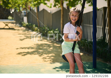 Cheerful Girl Enjoys Fun Play Activity on a Swing Outdoors in a Playground 129102286