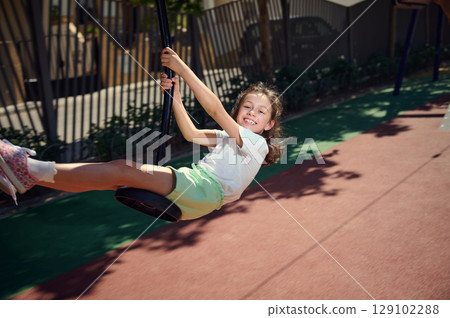 Excited Girl Playing on a Swing at a Sunny Playground 129102288
