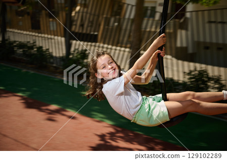 Smiling Child Enjoying a Swing Ride in a Sunny Playground 129102289