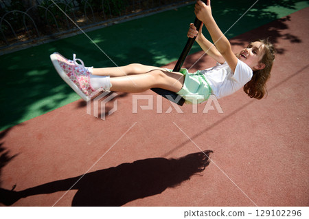 Young Girl Happily Swinging on Playground Swing During a Sunny Summer Day 129102296