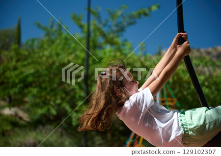 Smiling Girl Enjoying Summer Outdoor Playtime on a Swing in a Sunny Park Smiling Girl Enjoying Summer Outdoor Playtime on a Swing in a Sunny Park 129102307
