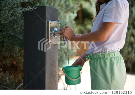 Child Collecting Water from Outdoor Tap in Summer 129102310