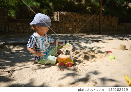 Young Child Enjoying a Summer Day Building Sand Castles in Playground Young Child Enjoying a Summer Day Building Sand Castles in Playground 129102319