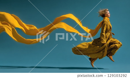 Fashion model jumping with flowing yellow fabric on blue background 129103292