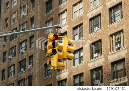 Traffic light prominently displays red, yellow, and green lights in busy city environment. Urban daytime setting enhances functional mood with building backdrop. 129103481