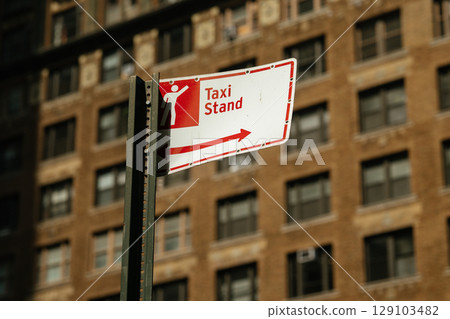 Urban taxi stand sign prominently displays pictogram of person and directional arrow. Bright daylight enhances informative and functional mood of city street setting. Urban taxi stand sign prominently displays pictogram of person and directional arrow. Bright daylight enhances informative and functional mood of city street setting. 129103482