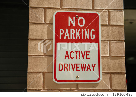 Outdoor sign displayed on brick wall serves as a cautionary message. Text reads 'NO PARKING' and 'ACTIVE DRIVEWAY', emphasizing the importance of following regulations in the area. Outdoor sign displayed on brick wall serves as a cautionary message. Text reads 'NO PARKING' and 'ACTIVE DRIVEWAY', emphasizing the importance of following regulations in the area. 129103483