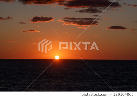 The sun setting over the sea and orange glowing clouds 129104005