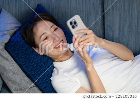 A woman lying on the sofa and looking at her smartphone 129105016