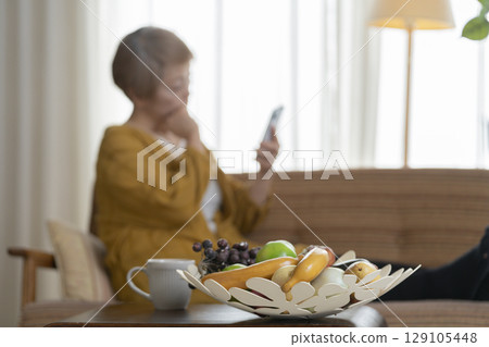 一位老婦人坐在沙發上,手裡拿著一支智慧型手機 一位老婦人坐在沙發上,手裡拿著一支智慧型手機 129105448