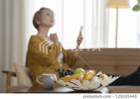 一位老婦人坐在沙發上,手裡拿著一支智慧型手機 一位老婦人坐在沙發上,手裡拿著一支智慧型手機 129105449