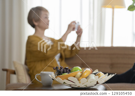 一位老婦人坐在沙發上，手裡拿著一支智慧型手機 129105450