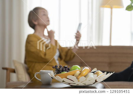 一位老婦人坐在沙發上，手裡拿著一支智慧型手機 129105451