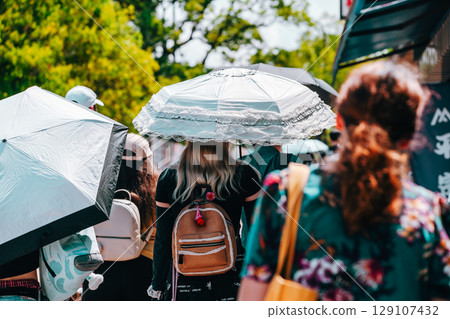 People walking with umbrellas on a sunny summer day 129107432