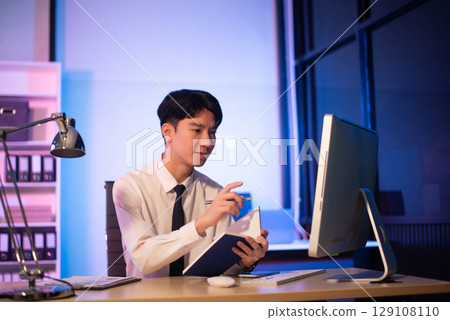 Businessman drinking coffee to get some energy for working overtime sitting at desk using computer and doing overtime Businessman drinking coffee to get some energy for working overtime sitting at desk using computer and doing overtime 129108110