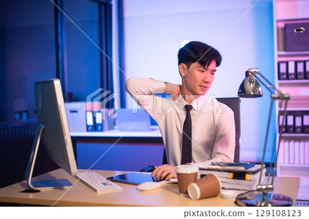 Overworked young Asian businesswoman office worker suffering from neck pain after had a long day at her office desk. Overworked young Asian businesswoman office worker suffering from neck pain after had a long day at her office desk. 129108123