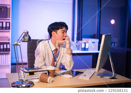 Businessman drinking coffee to get some energy for working overtime sitting at desk using computer and doing overtime 129108131