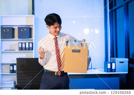 Asian male professional packing office belongings in a box, representing themes of resignation, new job, or relocation. Office, job, career change Asian male professional packing office belongings in a box, representing themes of resignation, new job, or relocation. Office, job, career change 129108268