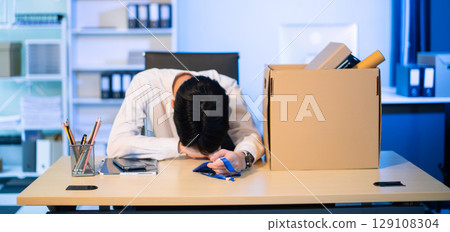 Asian male professional packing office belongings in a box, representing themes of resignation, new job, or relocation. Office, job, career change Asian male professional packing office belongings in a box, representing themes of resignation, new job, or relocation. Office, job, career change 129108304