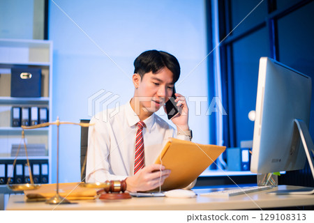 Young Asian lawyer at desk with legal scales and gavel, writing documents in office, offering legal services Young Asian lawyer at desk with legal scales and gavel, writing documents in office, offering legal services 129108313