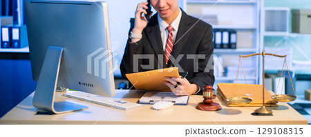 Young Asian lawyer at desk with legal scales and gavel, writing documents in office, offering legal services 129108315