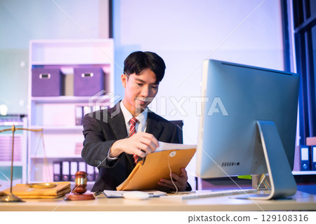 Young Asian lawyer at desk with legal scales and gavel, writing documents in office, offering legal services Young Asian lawyer at desk with legal scales and gavel, writing documents in office, offering legal services 129108316