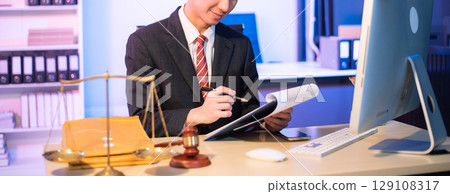 Young Asian lawyer at desk with legal scales and gavel, writing documents in office, offering legal services Young Asian lawyer at desk with legal scales and gavel, writing documents in office, offering legal services 129108317