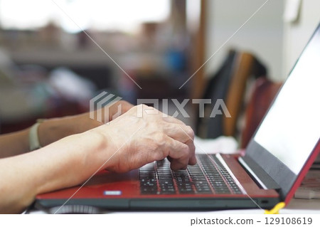 Hands of an elderly woman operating a computer 129108619