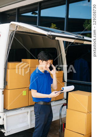 Asian courier delivery man searching the address on digital tablet.  near van outside the warehouse. 129108730