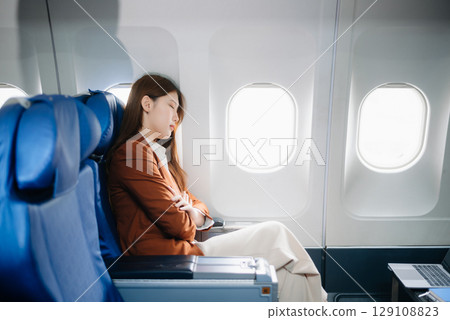 Photo of a frustrated woman sitting on an airplane with her head in her hands. Asian woman sitting in a seat 129108823