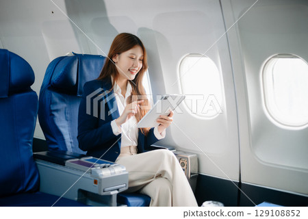 Young Asian executive excels in first class, multitasking with digital tablet, laptop and smartphone. Travel in style, work 129108852