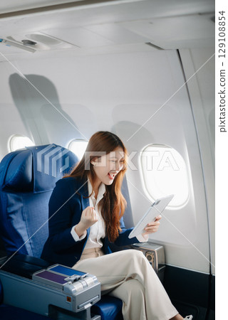 Young Asian executive excels in first class, multitasking with digital tablet, laptop and smartphone. Travel in style, work Young Asian executive excels in first class, multitasking with digital tablet, laptop and smartphone. Travel in style, work 129108854