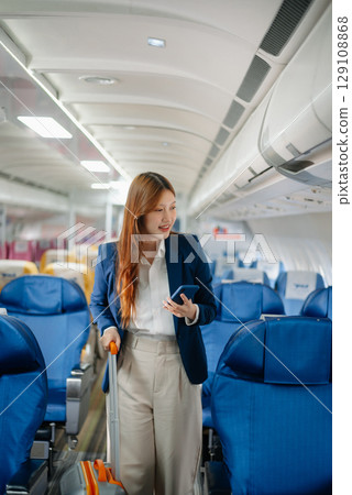 Attractive Asian female passenger of airplane sitting in comfortable seat while working laptop and tablet with mock up area using wireless connection. 129108868