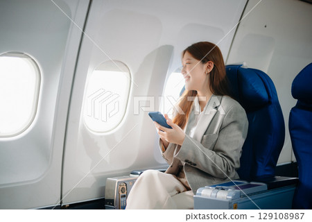 Portrait of a successful Asian businesswoman or entrepreneur in a formal suit on an airplane sitting in business class using a phone, computer laptop. Travel in style, work Portrait of a successful Asian businesswoman or entrepreneur in a formal suit on an airplane sitting in business class using a phone, computer laptop. Travel in style, work 129108987