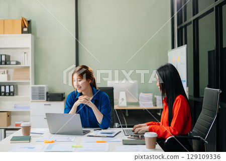 Two young Asian professionals engaged in teamwork and business discussions in modern office Two young Asian professionals engaged in teamwork and business discussions in modern office 129109336