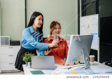 Two young Asian professionals engaged in teamwork and business discussions in modern office 129109448