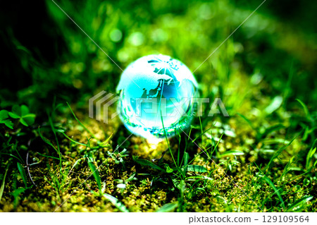 A beautiful globe crystal in the grass. Ecological image. Center position. Emerald green daytime color. 129109564