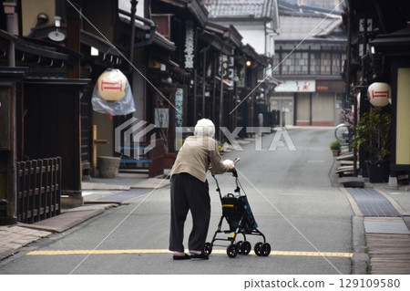 Old townscape of Takayama City, Gifu Prefecture, Japan. Historical old houses and decorative lanterns. An old woman taking a morning walk during the Takayama Spring Festival. 129109580