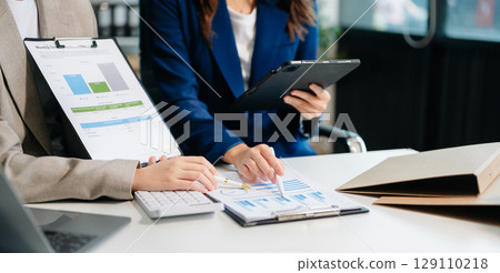 Business documents on office table with smart phone and calculator digital tablet and graph business with social network diagram and two colleagues discussing data working 129110218
